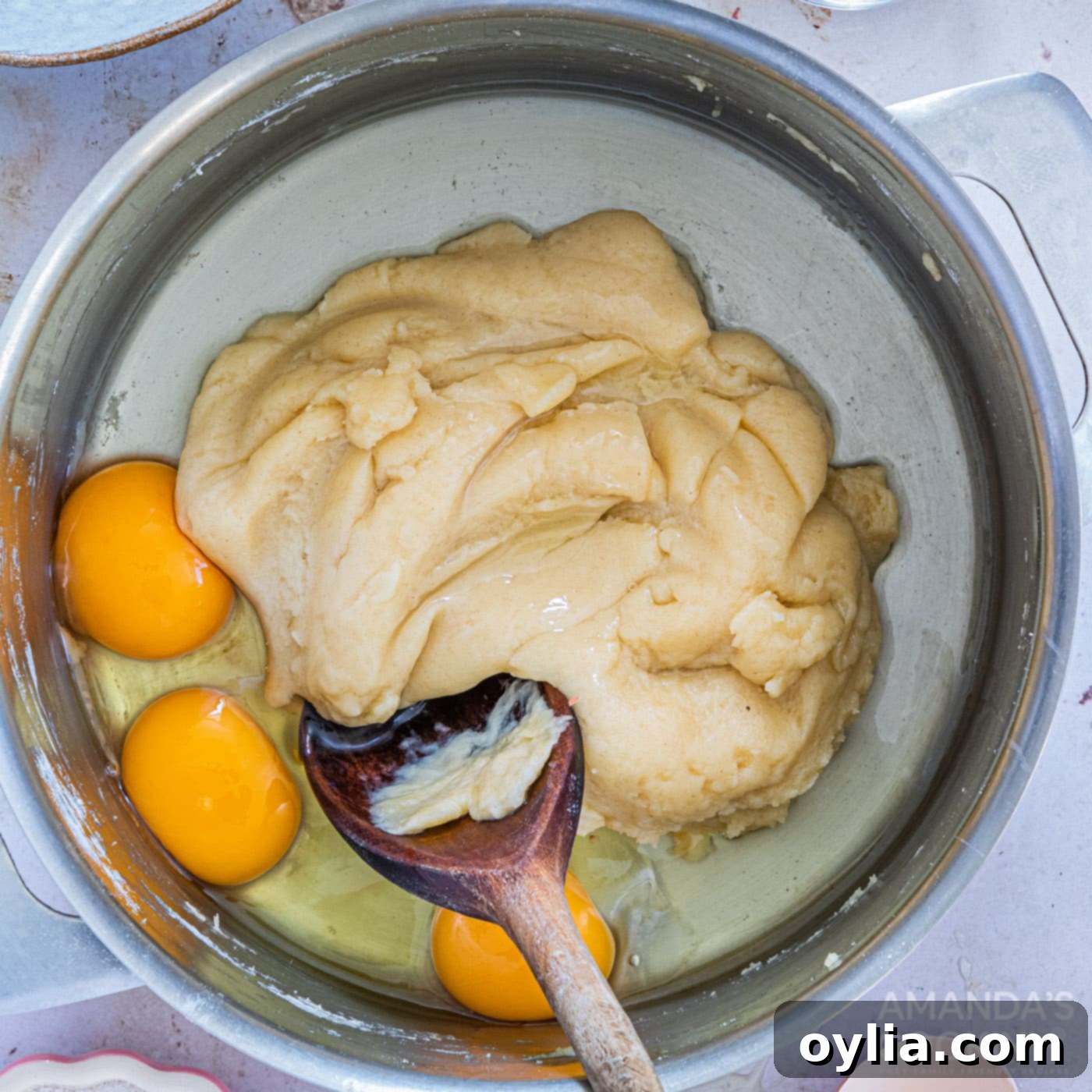 Whisking eggs into the cooled churro dough batter to create a smooth, sticky consistency.