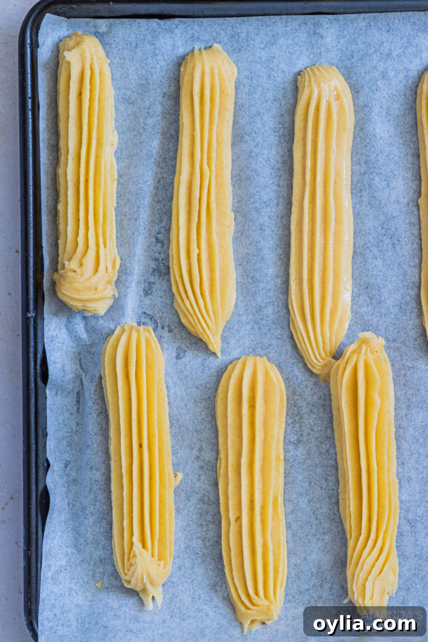 Piped churro dough neatly arranged on a parchment-lined baking sheet, ready for freezing.