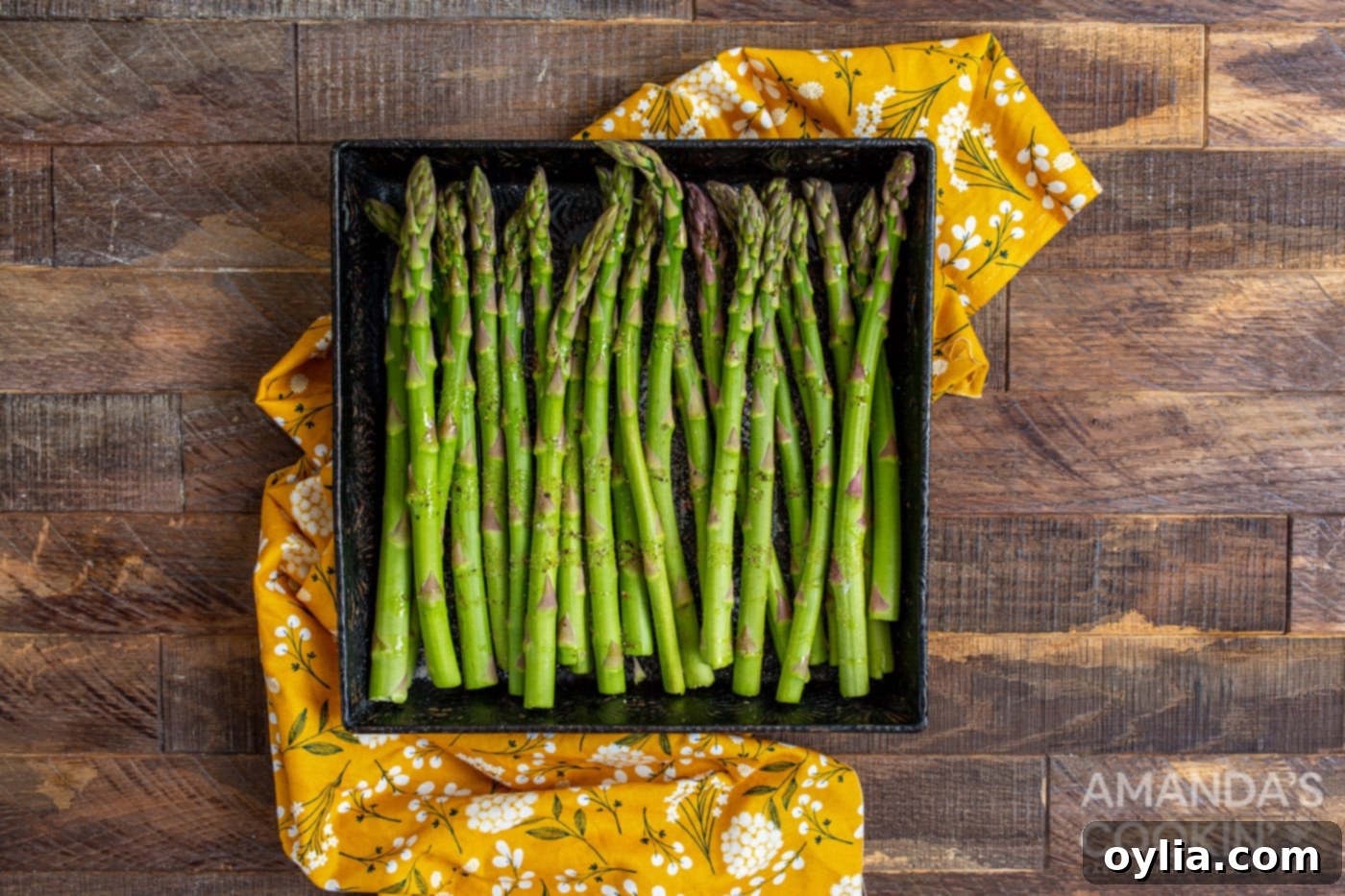 asparagus in a casserole dish being tossed with olive oil, salt, and pepper
