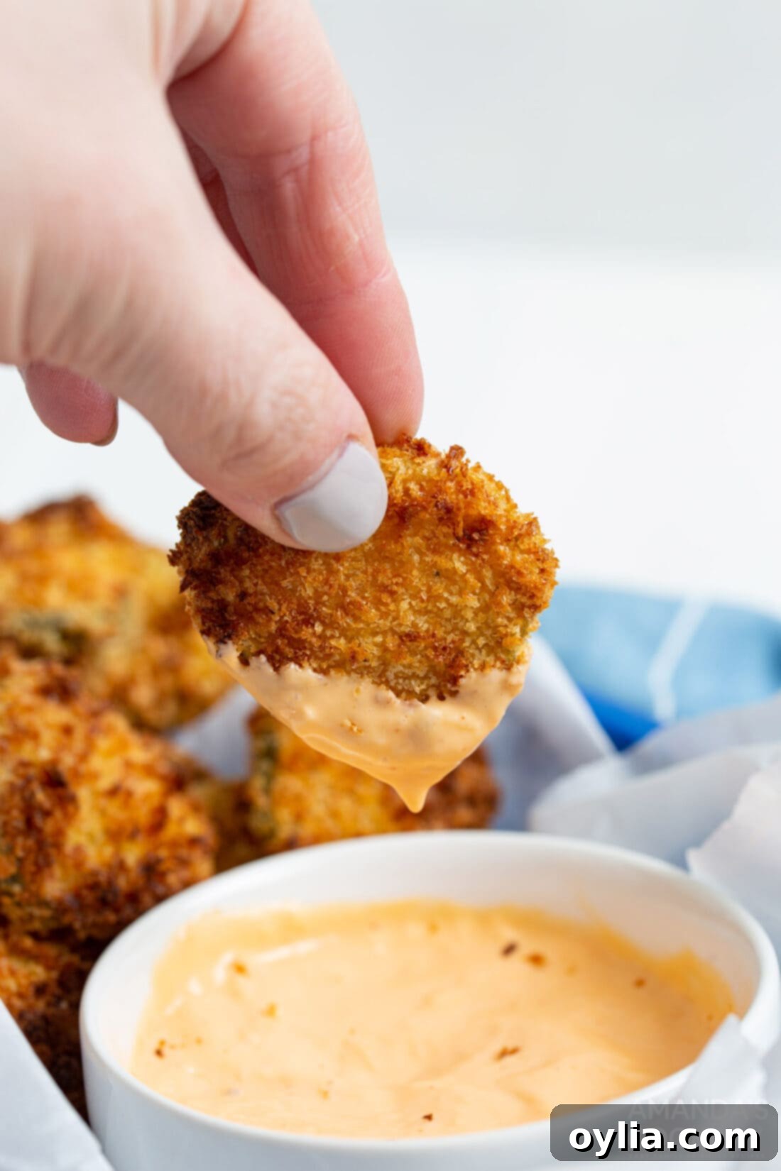 A crispy golden brown air fryer fried pickle being dipped into a creamy sauce.