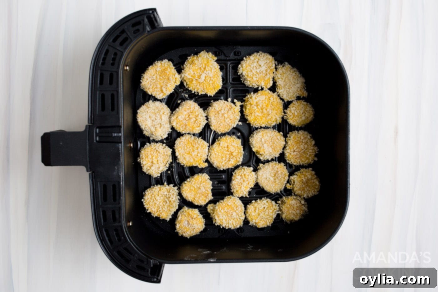 Panko coated pickle chips arranged in a single layer in an air fryer basket, lightly sprayed with cooking oil.
