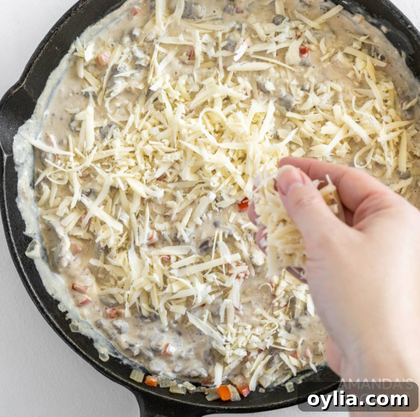 topping Philly cheesesteak dip with cheese in a skillet
