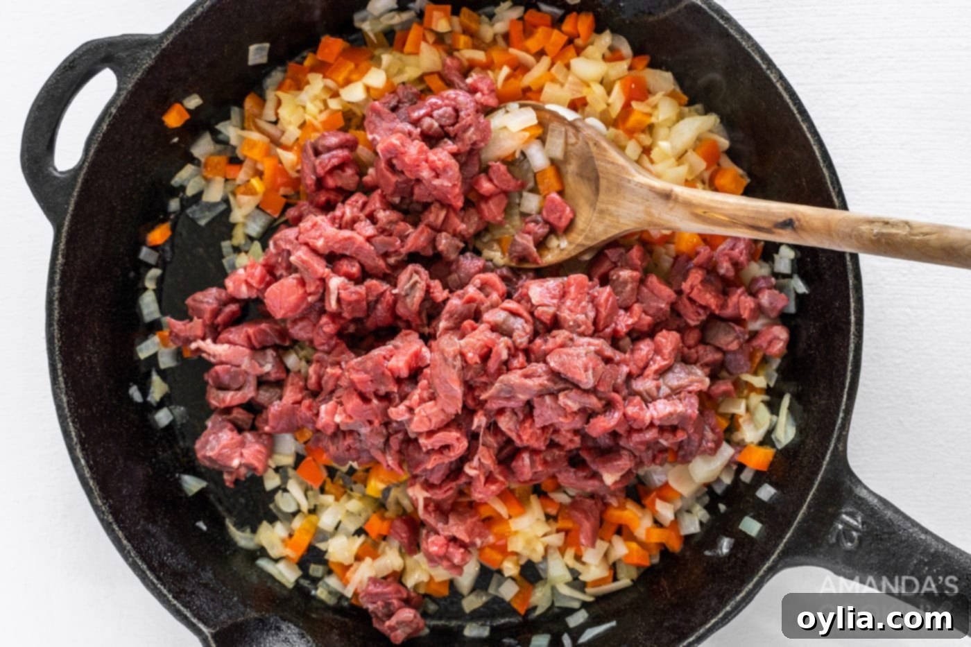 chopped steak on top of veggies in cast iron skillet