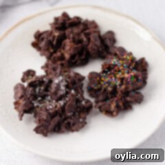 A stack of golden brown cornflake cookies drizzled with white chocolate on a decorative plate.