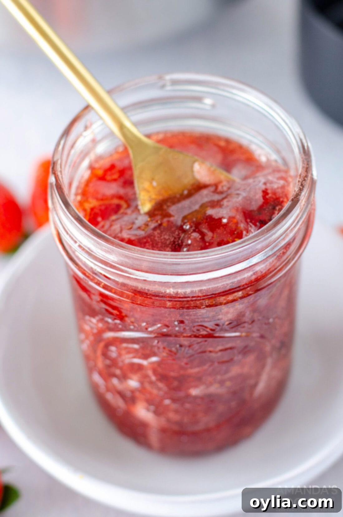 Jar of Strawberry Jam with a spoon in it, showcasing its rich red color and chunky texture.