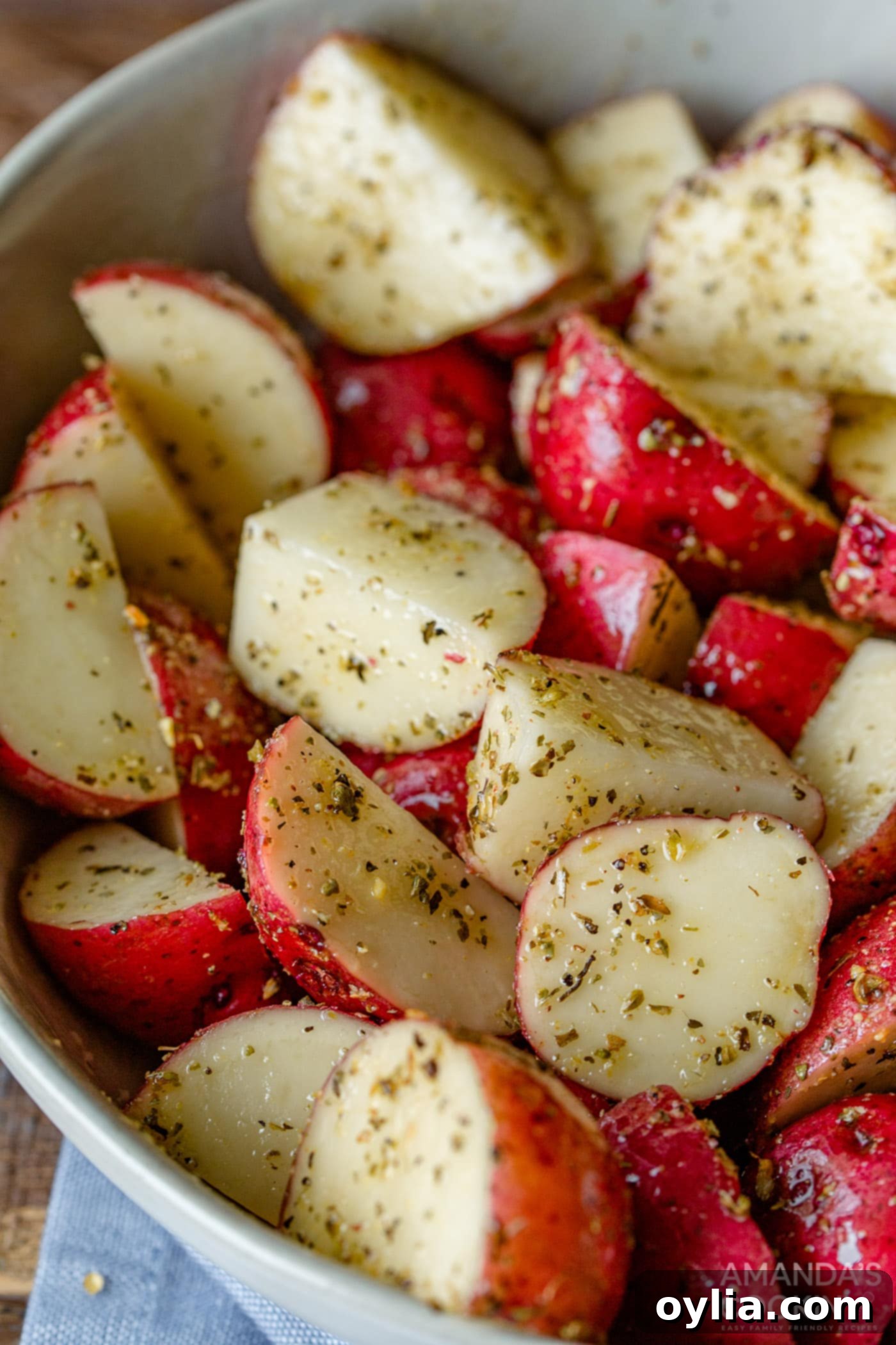 Cubed potatoes in a mixing bowl, generously coated with olive oil and a blend of seasonings, ready for the air fryer.