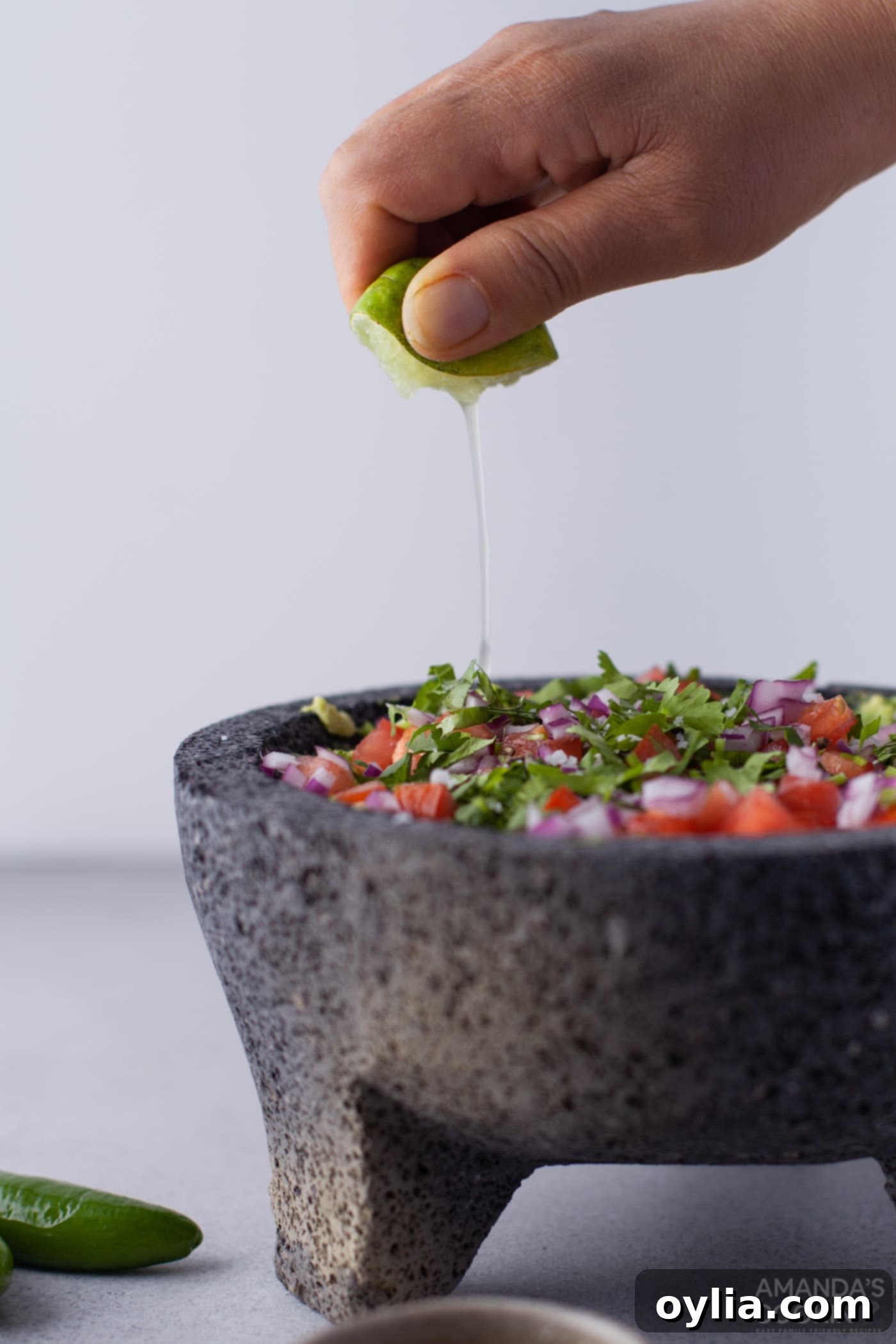 Hand squeezing fresh lime into guacamole in a molcajete