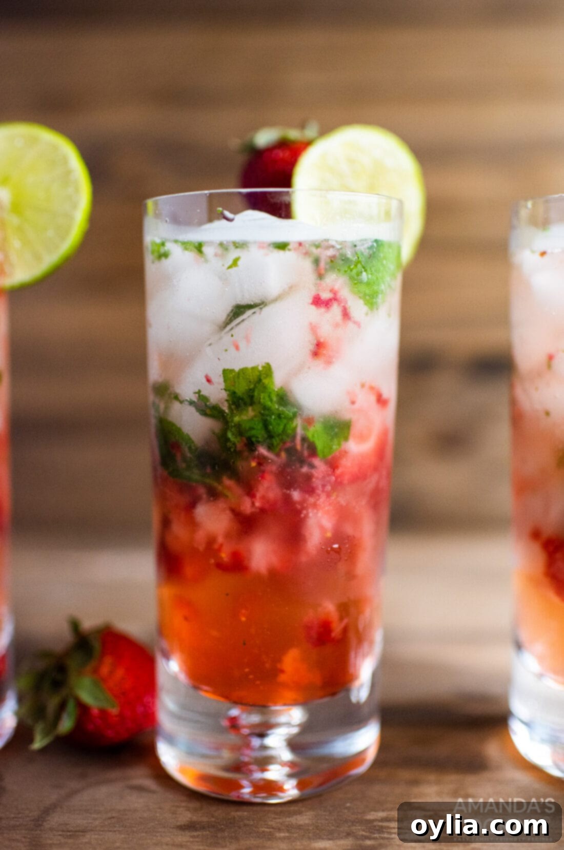 A vibrant strawberry mojito cocktail in a glass, garnished with fresh mint and a lime wedge.