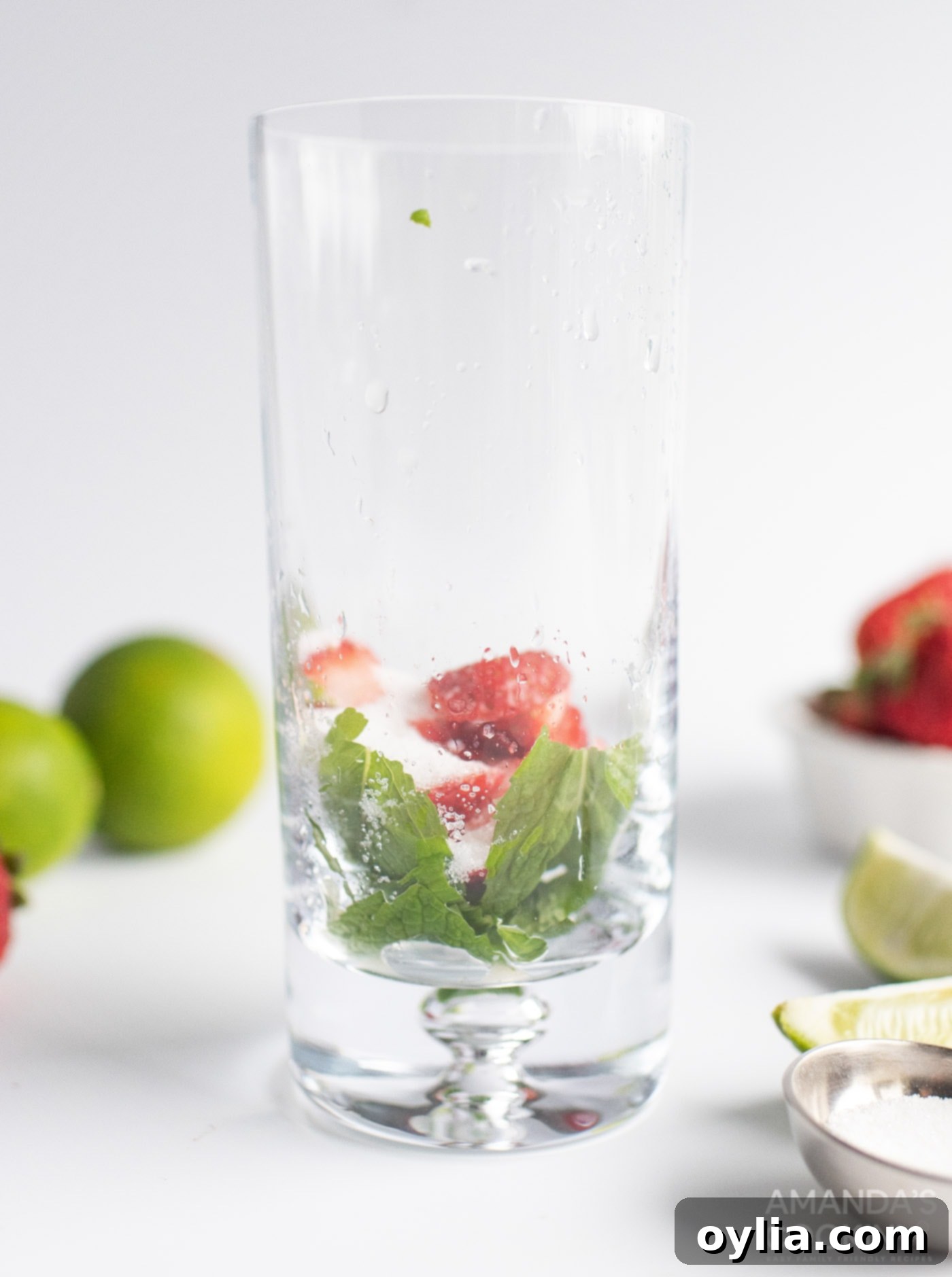 Mint leaves and sliced strawberries being muddled in a highball glass.