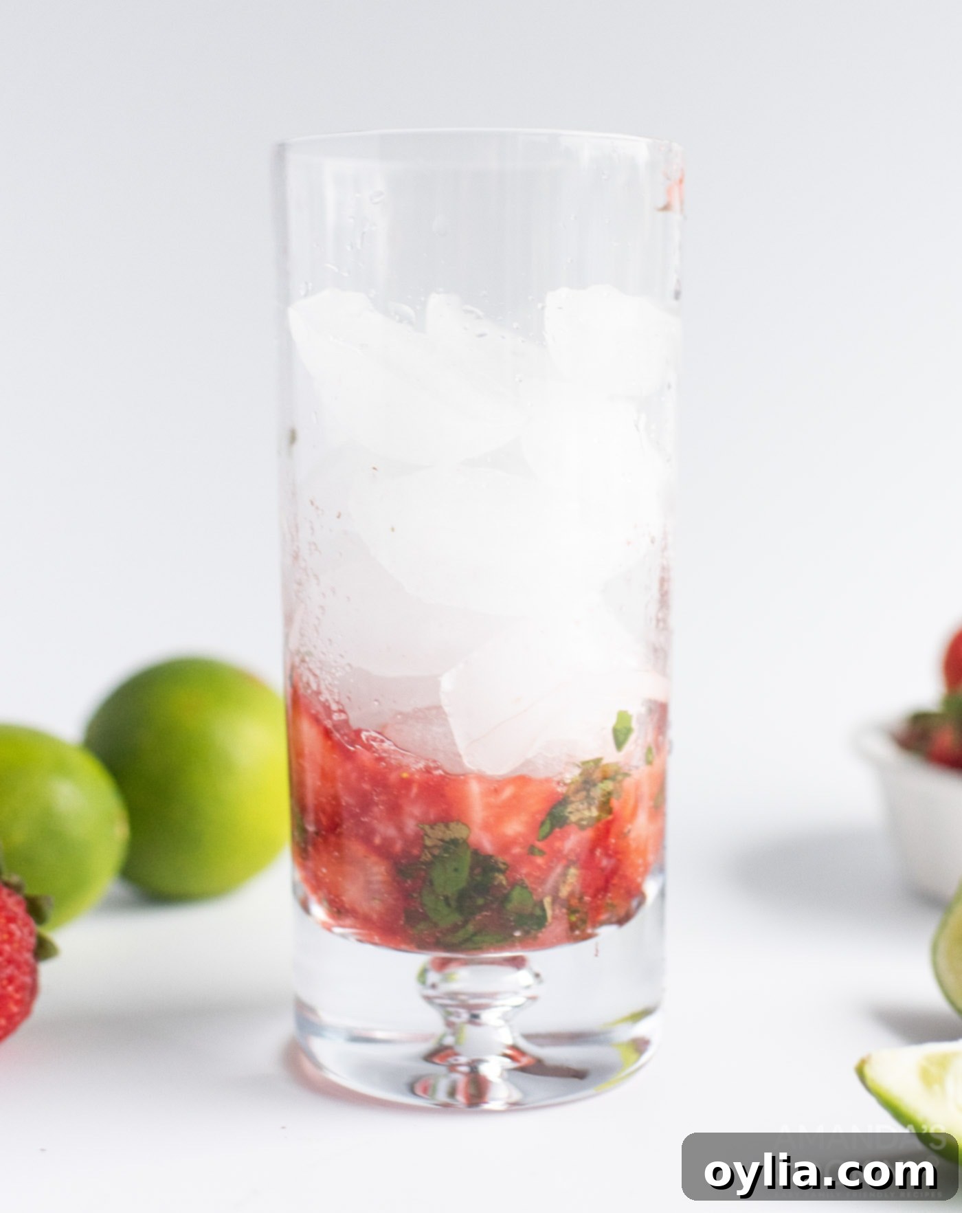 Muddled strawberries and mint in a glass, with lime juice and sugar added, ready for the next step.