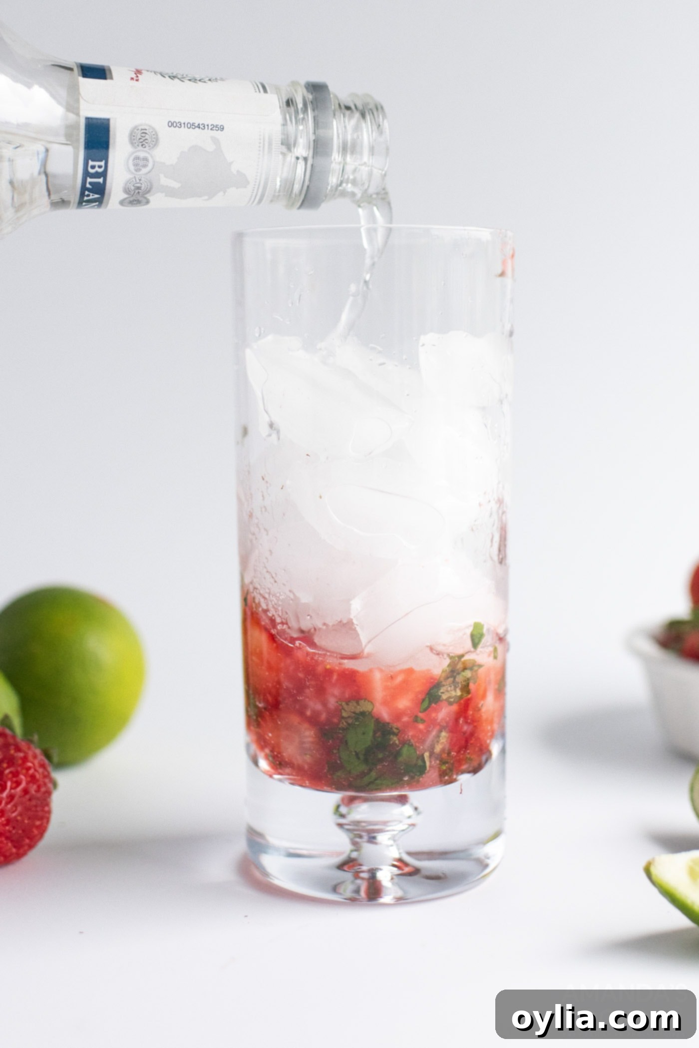 Pouring club soda into a highball glass filled with ice, muddled strawberries, mint, and rum.