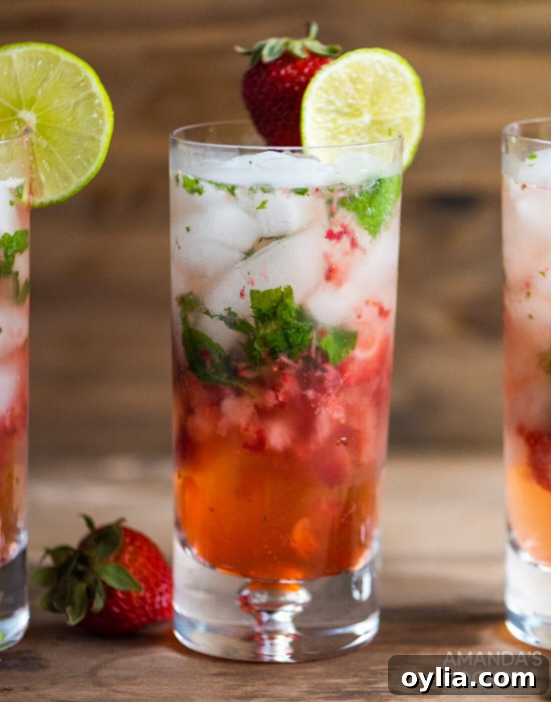 A close-up of a refreshing Strawberry Mojito cocktail with condensation on the glass, garnished with lime and mint.