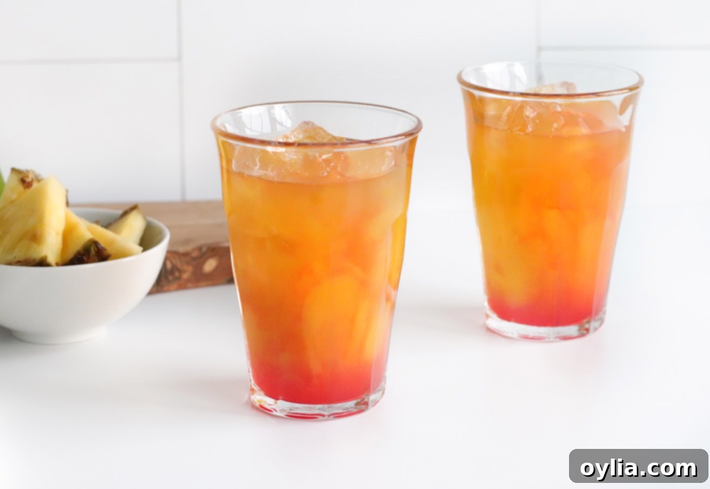 Grenadine being added to the layers of pineapple juice, mango juice, and rum in a glass