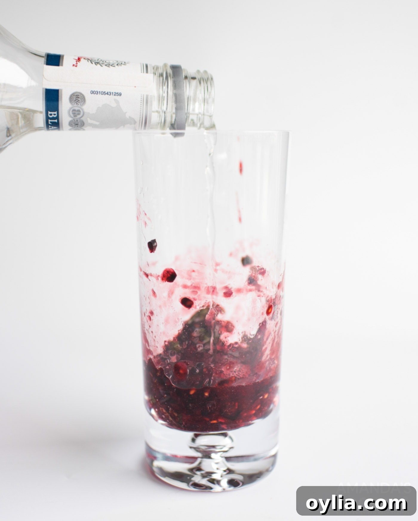 Pouring rum into muddle blackberries and mint in a glass