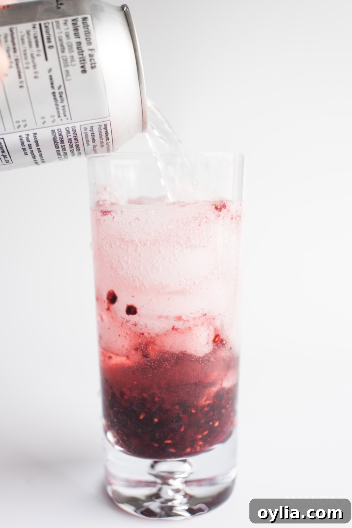 pouring club soda into a glass of blackberry mojito