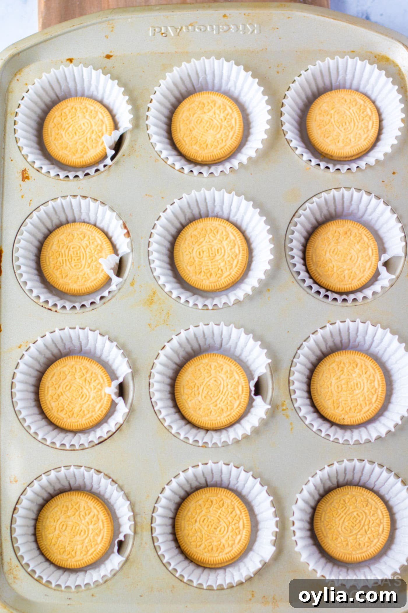 Golden Oreo cookies neatly placed into each cupcake liner within a muffin tin, forming the crusts for mini cheesecakes.