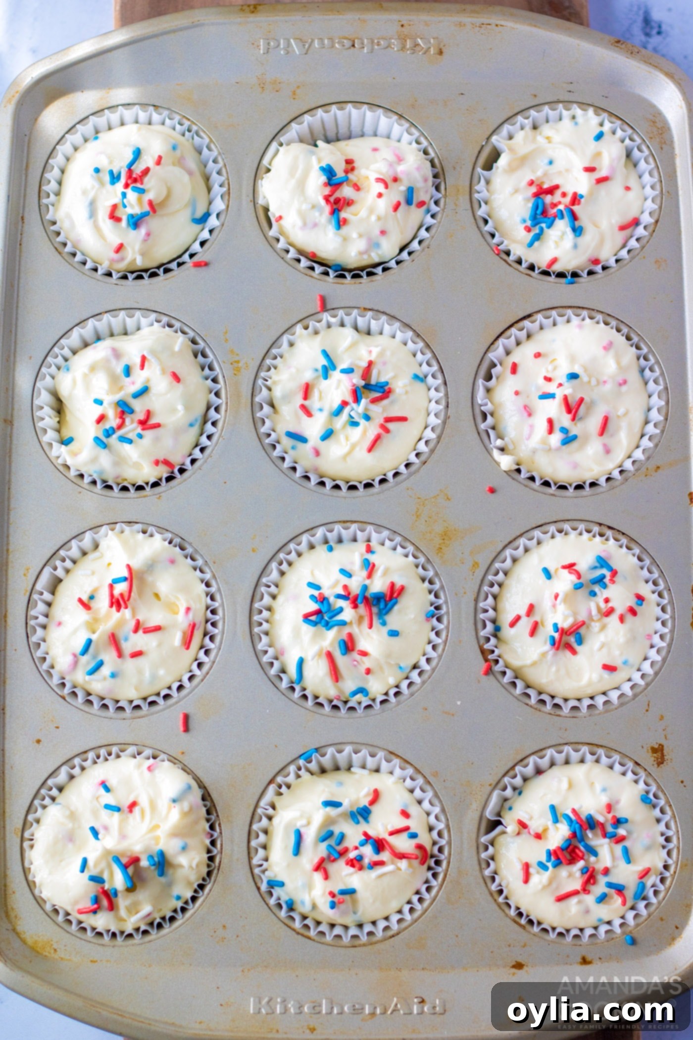 Mini cheesecake batter in a muffin tin, generously topped with red, white, and blue sprinkles before baking.