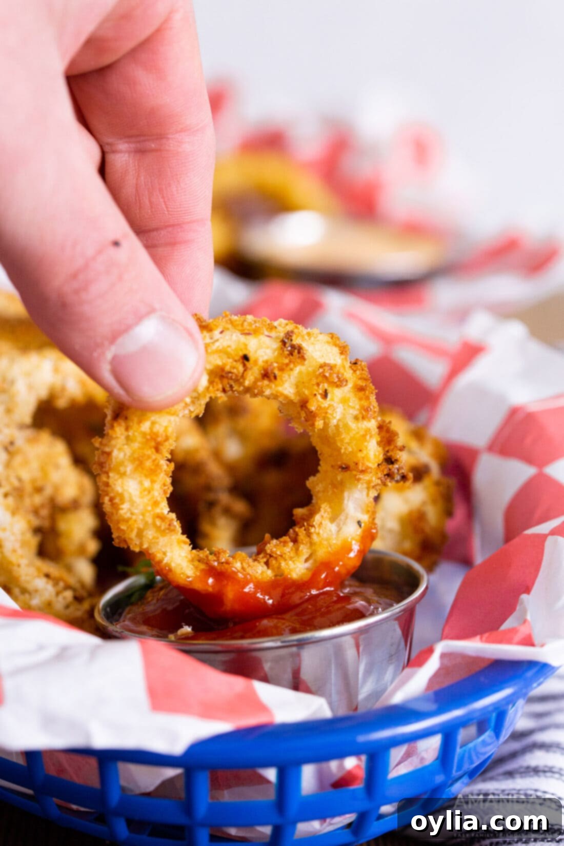 Hand dipping a golden air fryer onion ring into a bowl of ketchup