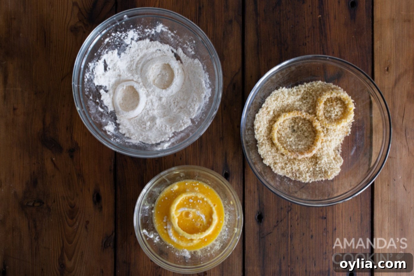 Dipping an onion ring into bowls of flour, whisked eggs, and seasoned panko breadcrumbs
