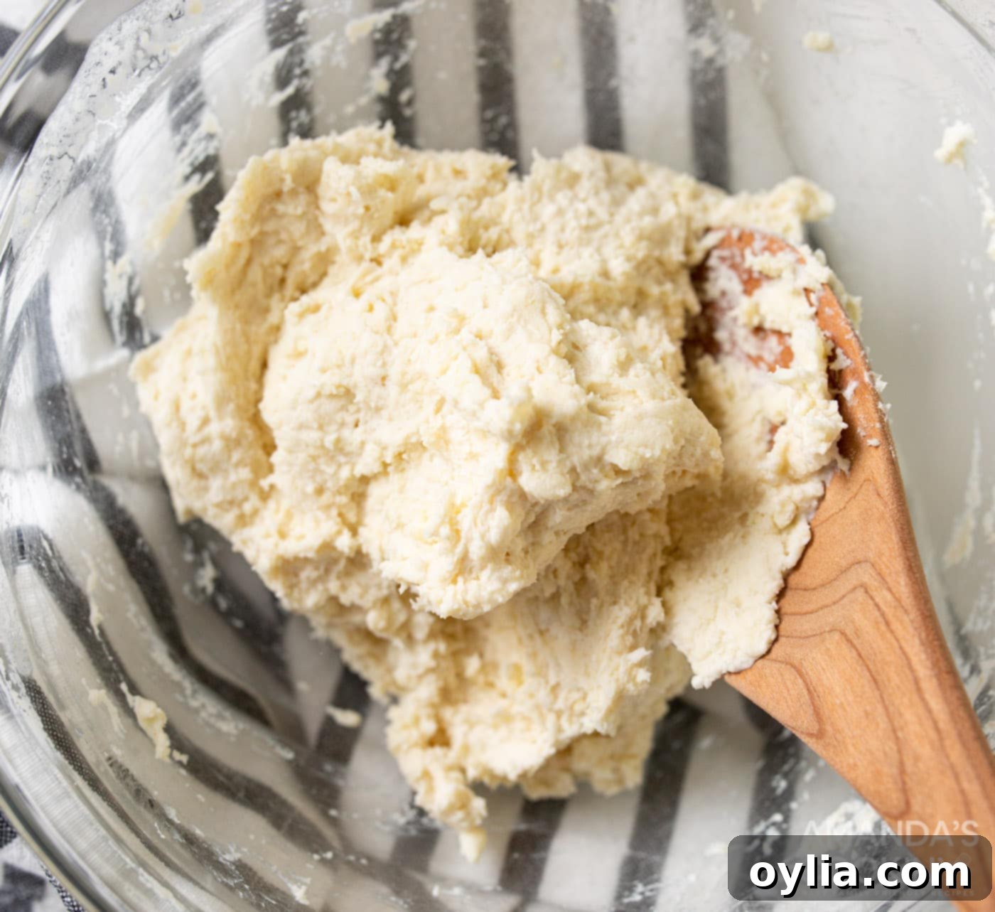 Pie dough in a bowl with a wooden spoon, indicating it's ready for rolling