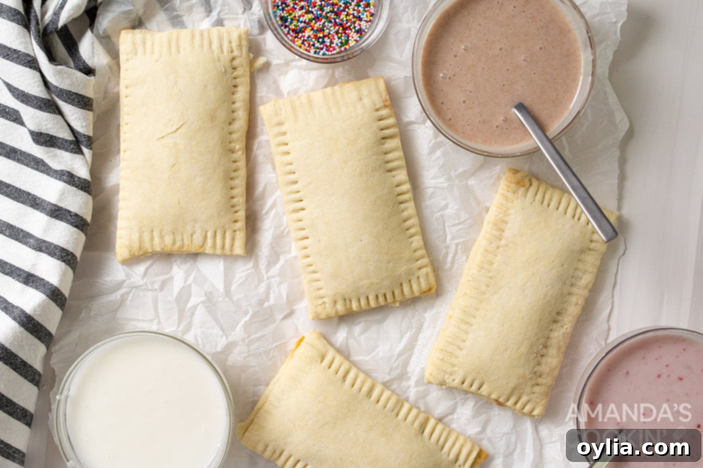 Baked pop tarts cooling on a baking sheet, with a bowl of glaze nearby