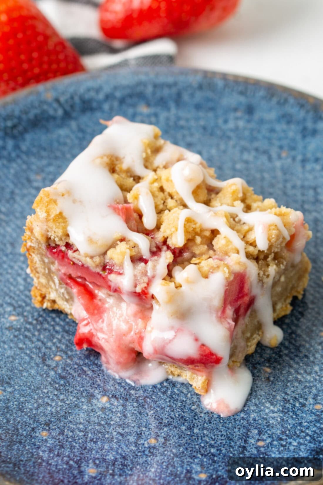 Close up photo of a Strawberry Rhubarb Crumble Bar on a blue plate, showing the layers of fruit and crumble.
