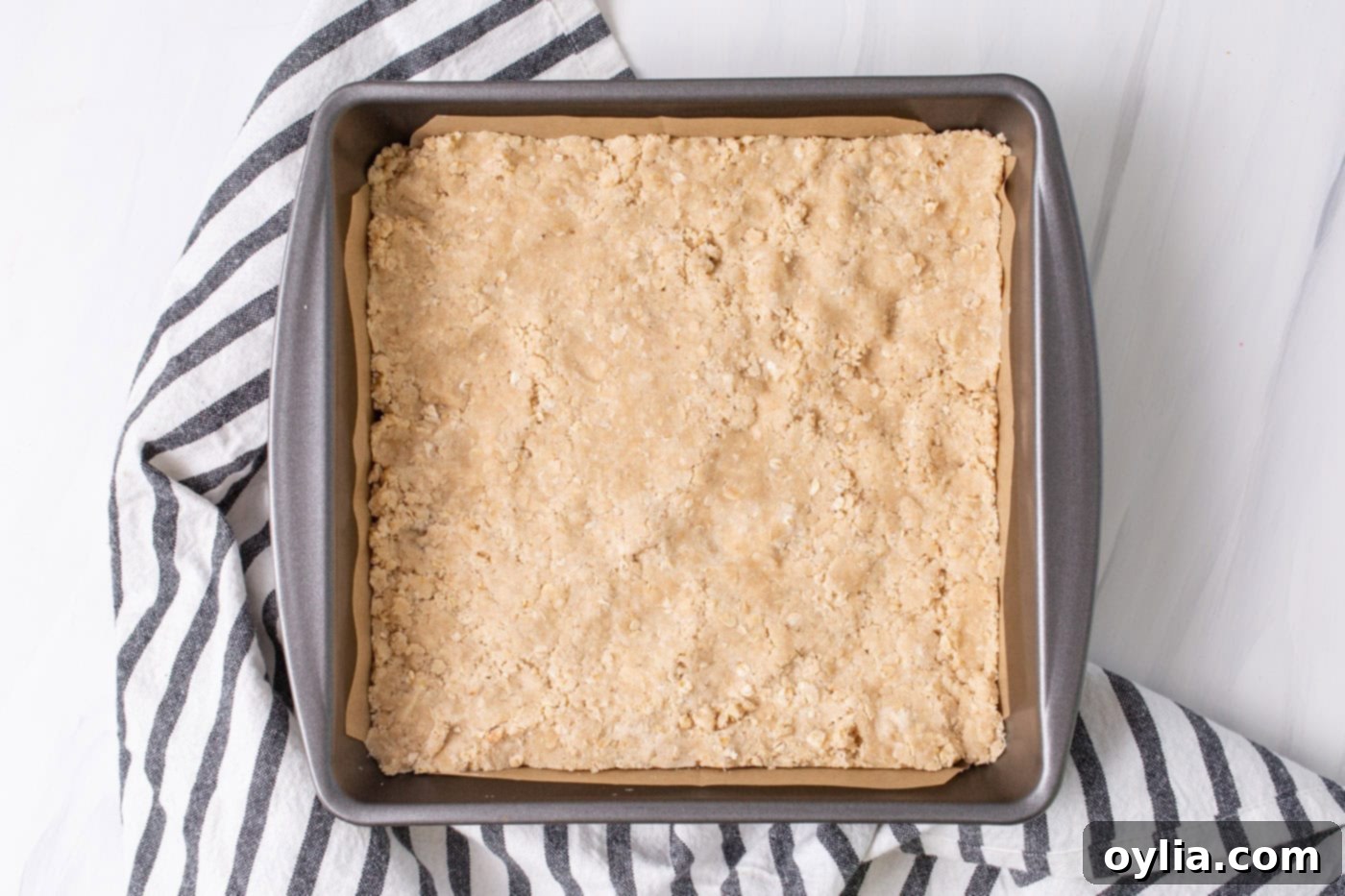 Rhubarb crumble bars crust in a parchment-lined 8x8 pan, pressed down evenly.