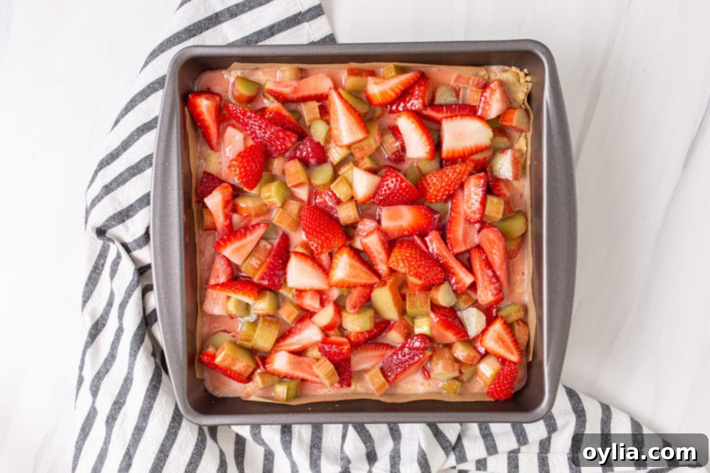 Strawberries and rhubarb fruit filling spread over the crumble crust in a baking pan.
