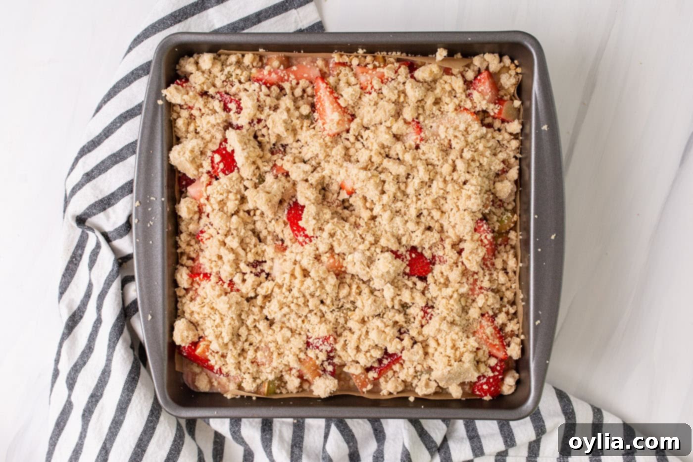 Crumble topping spread over the strawberry rhubarb filling in the pan, ready for baking.
