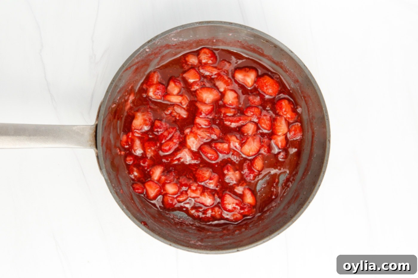 Homemade strawberry sauce simmering in a saucepan, thickening on the stove.