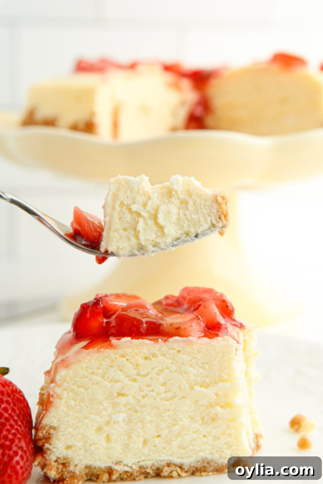 A fork taking a bite out of a slice of Instant Pot Strawberry Cheesecake, showing its creamy layers and strawberry topping.