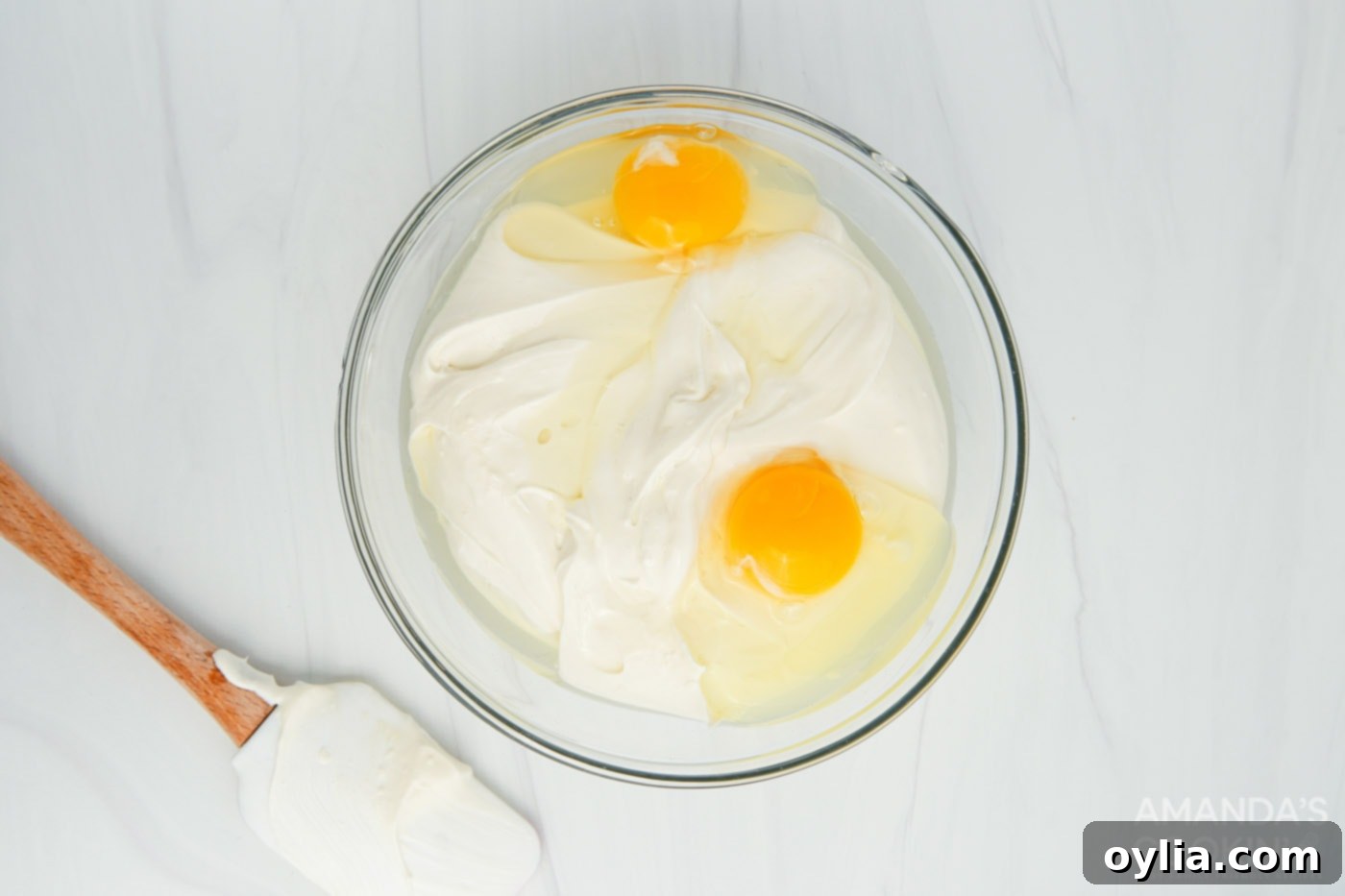 Creamy cheesecake batter with eggs, cream cheese, and sour cream being mixed in a large bowl with an electric mixer.