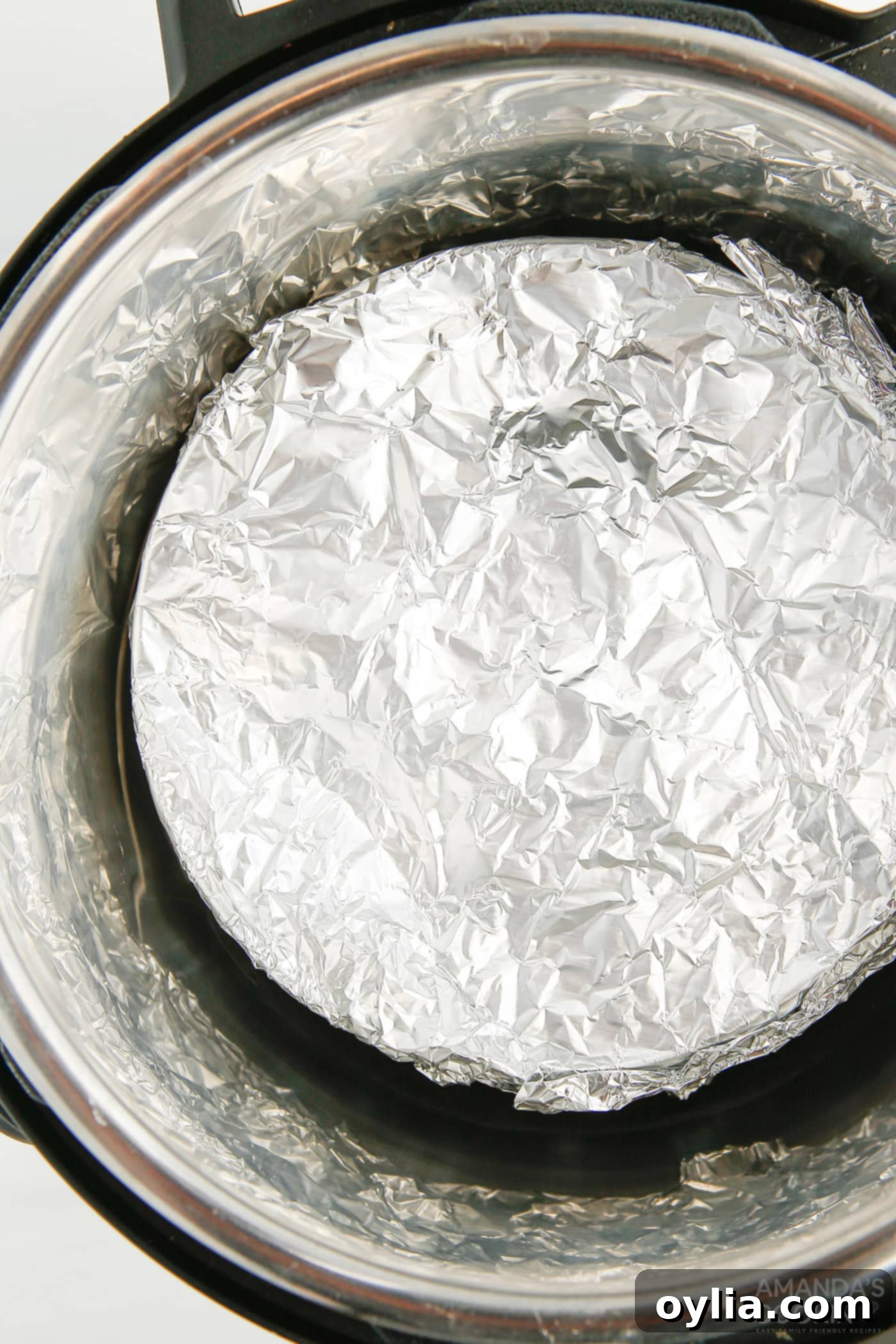 A springform pan covered in aluminum foil placed on a trivet inside an Instant Pot, ready for pressure cooking.