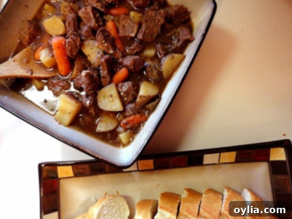 An overhead photo of beef stew with parsley, sage, rosemary and thyme in a square bowl.