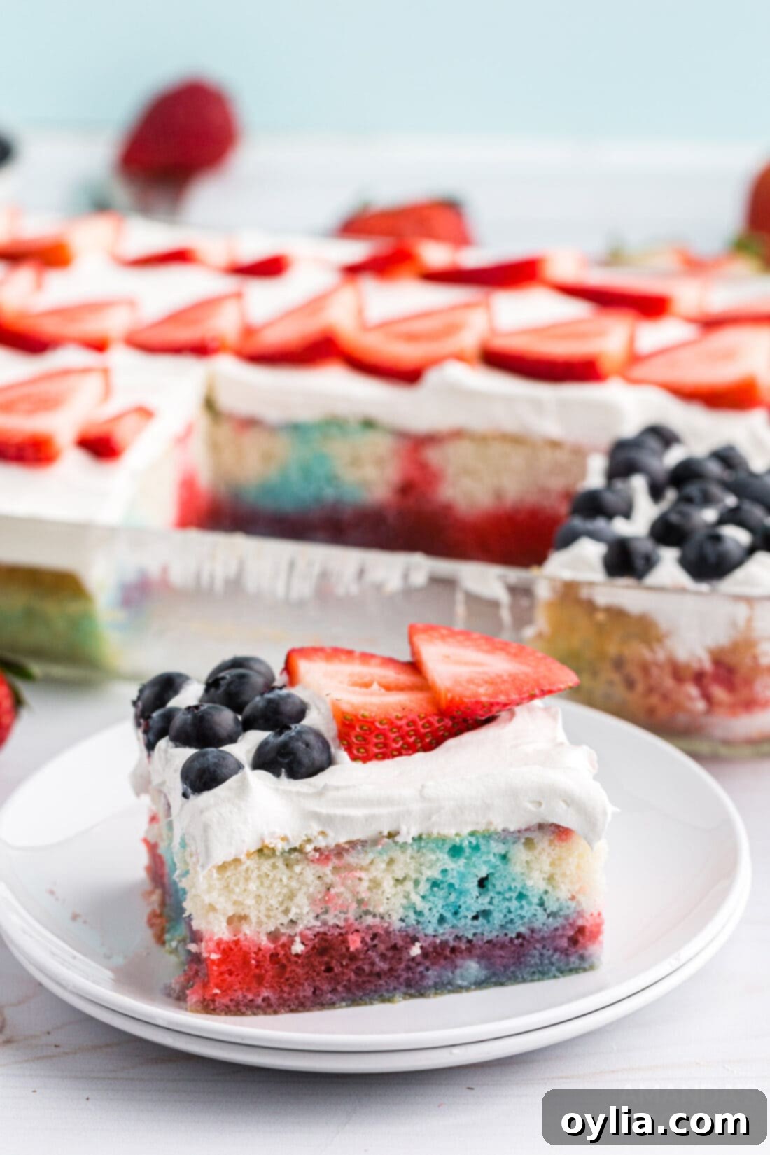Close-up slice of red white and blue poke cake showing layers of cake, jello, and berries