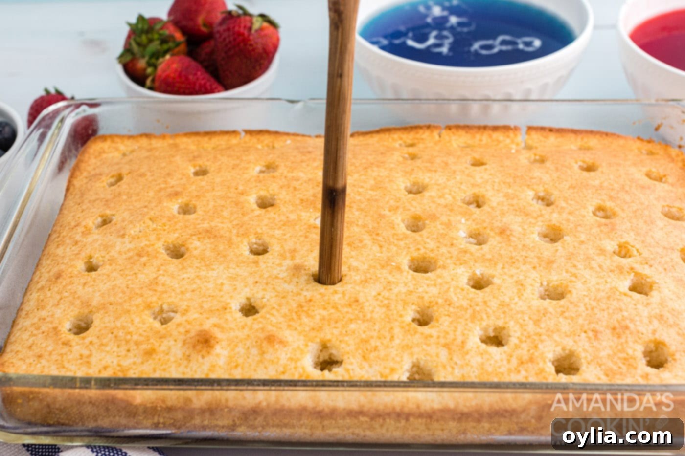 Poking holes into a warm white cake with a wooden spoon handle
