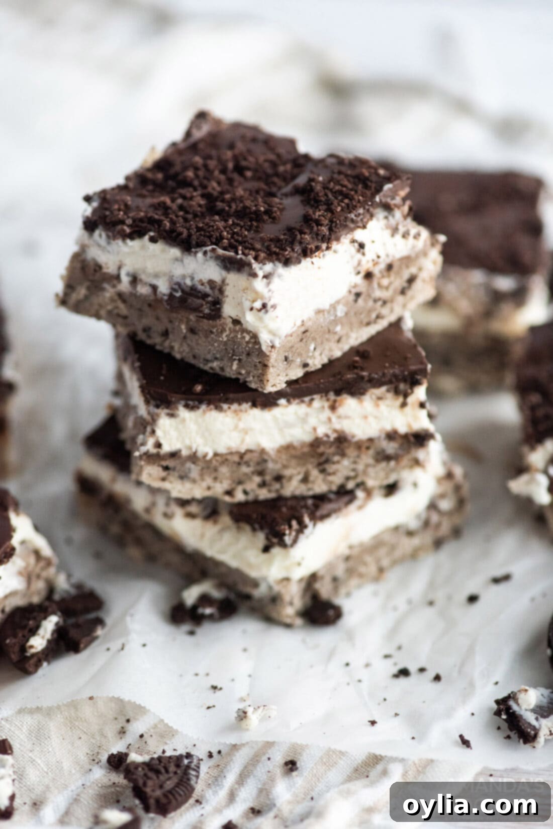A stack of golden-brown Oreo cheesecake bars, showcasing the distinct layers of cake, cheesecake, and chocolate ganache