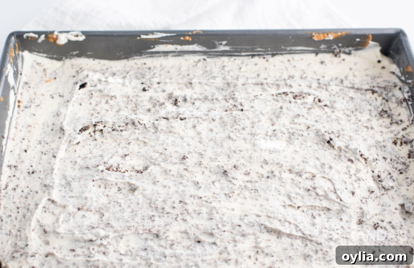 A top-down view of the Oreo cheesecake mixture in a pan, with cookie pieces visible within the creamy layer.