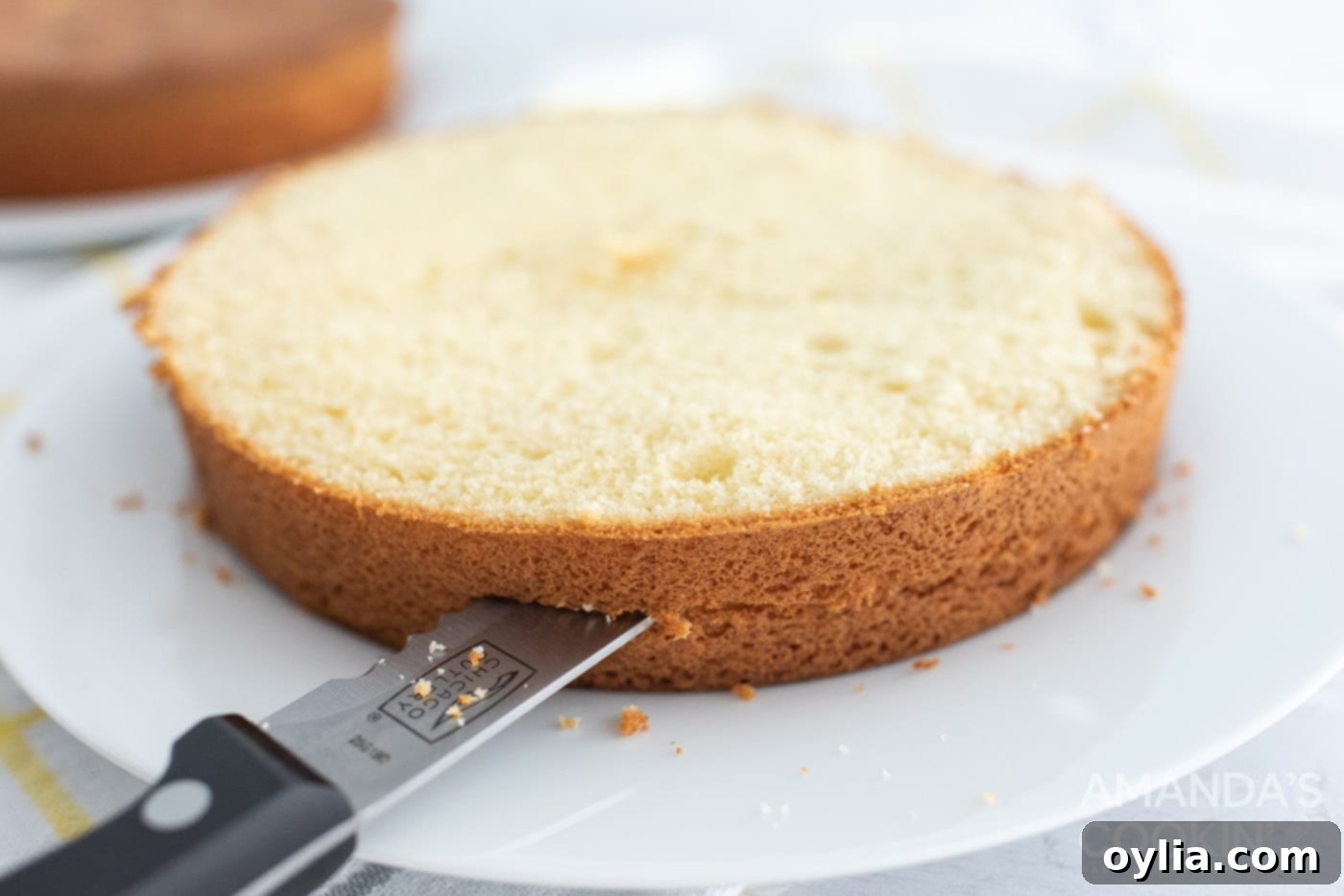 A knife carefully slicing a cooled cake layer horizontally, preparing it for multi-layer assembly.