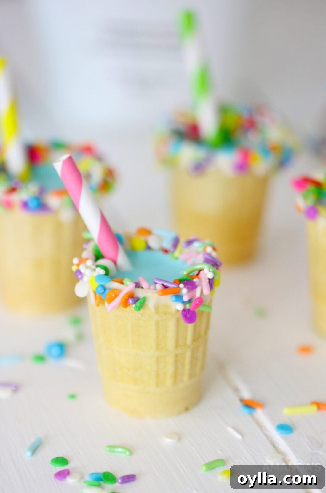Close-up of three RumChata Shots in ice cream cones, garnished with sprinkles and straws