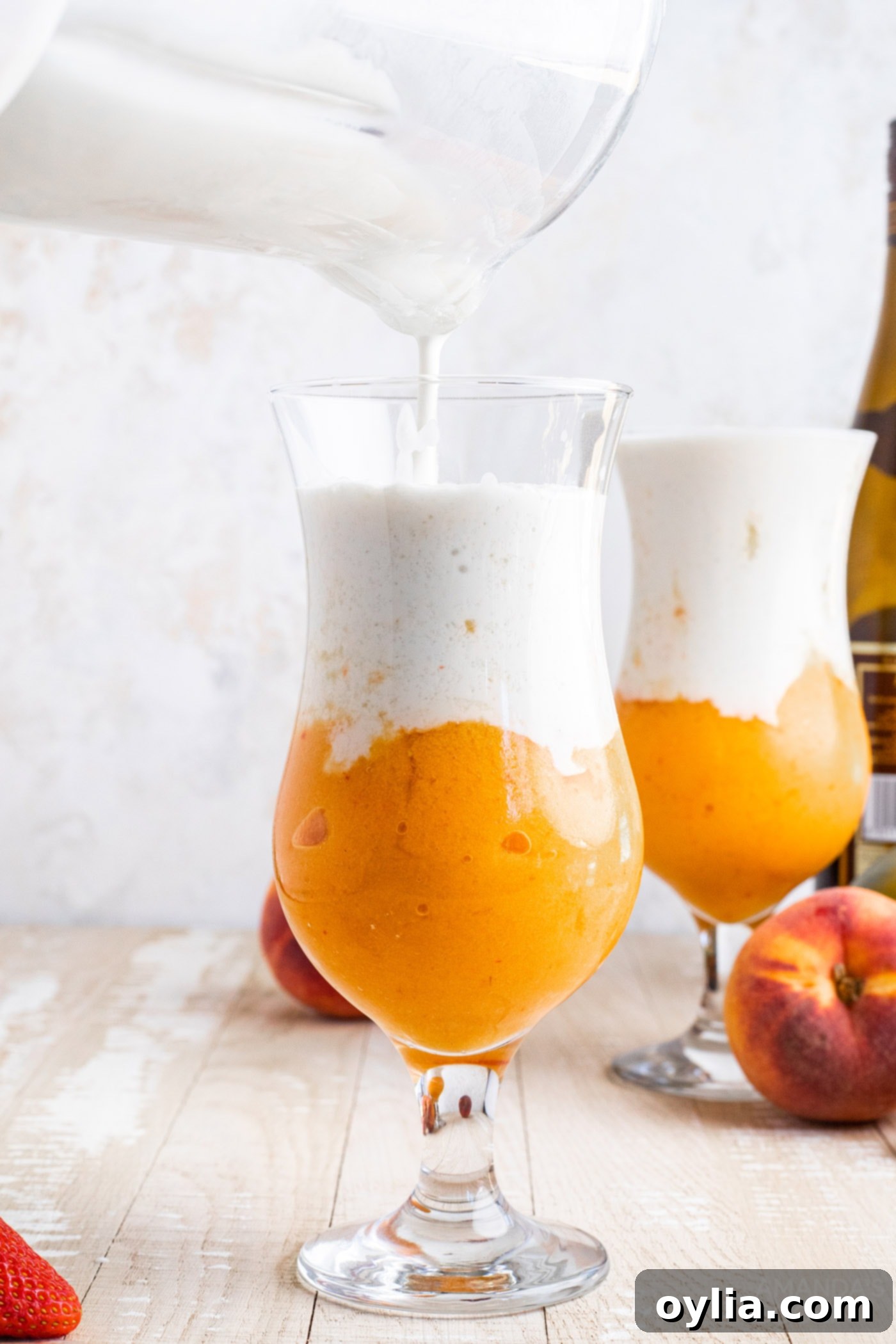 pouring coconut cream slush into fruit slush in a glass