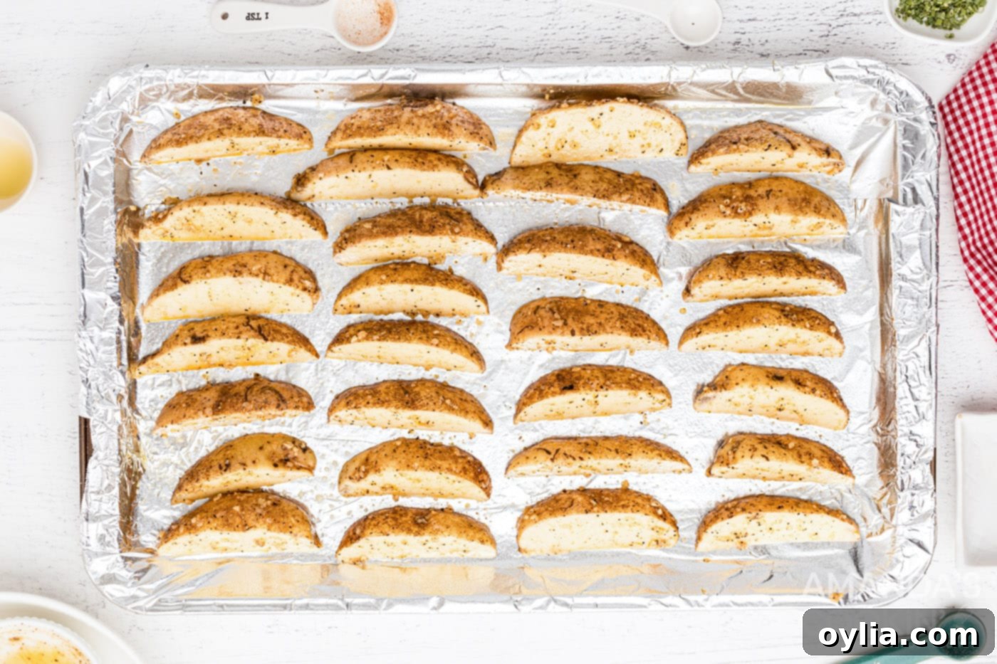 Seasoned potato wedges spread on a foil-lined baking sheet