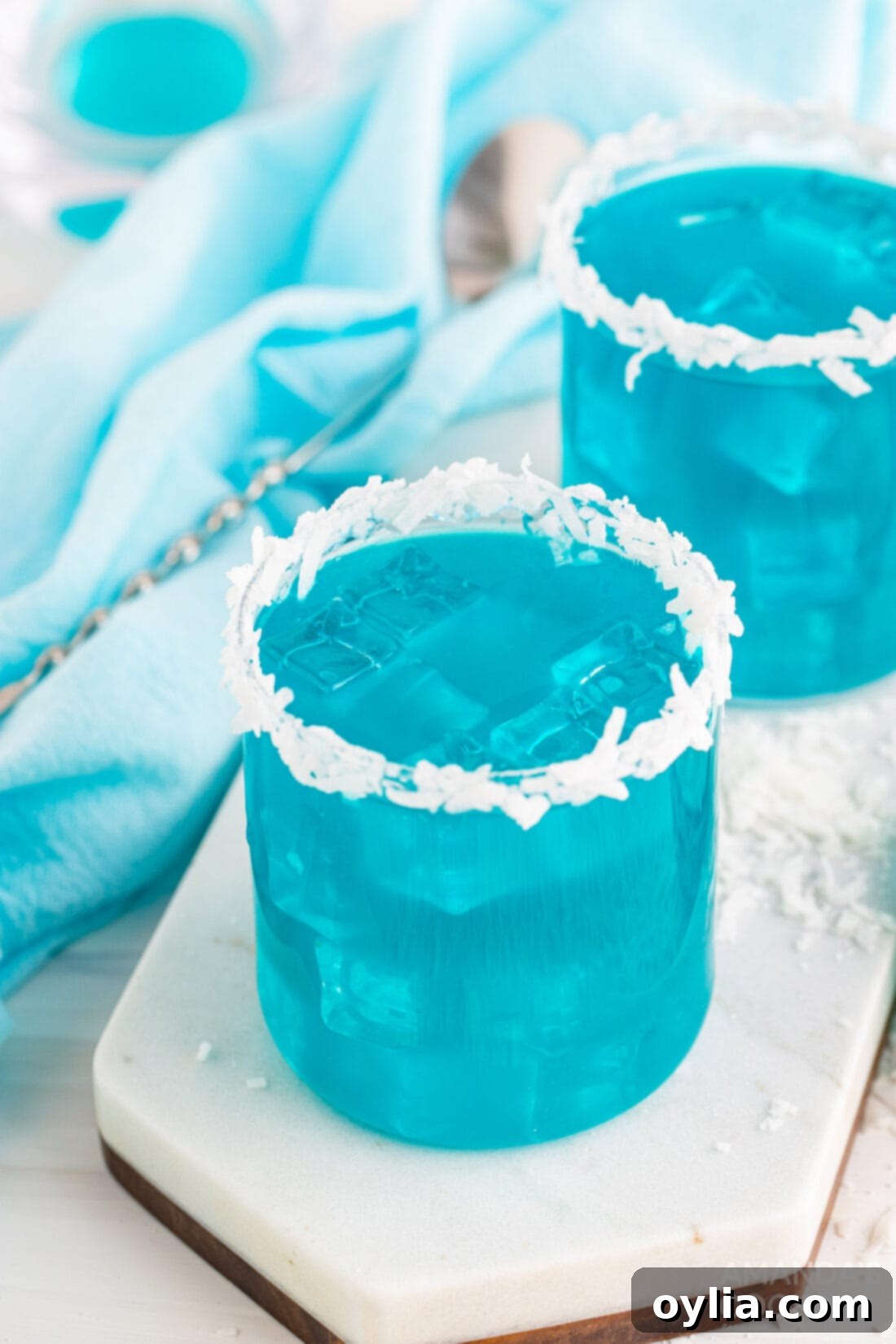 Two glasses of sparkling blue Ocean Water Cocktail, garnished with pineapple wedges, inviting a refreshing tropical experience.