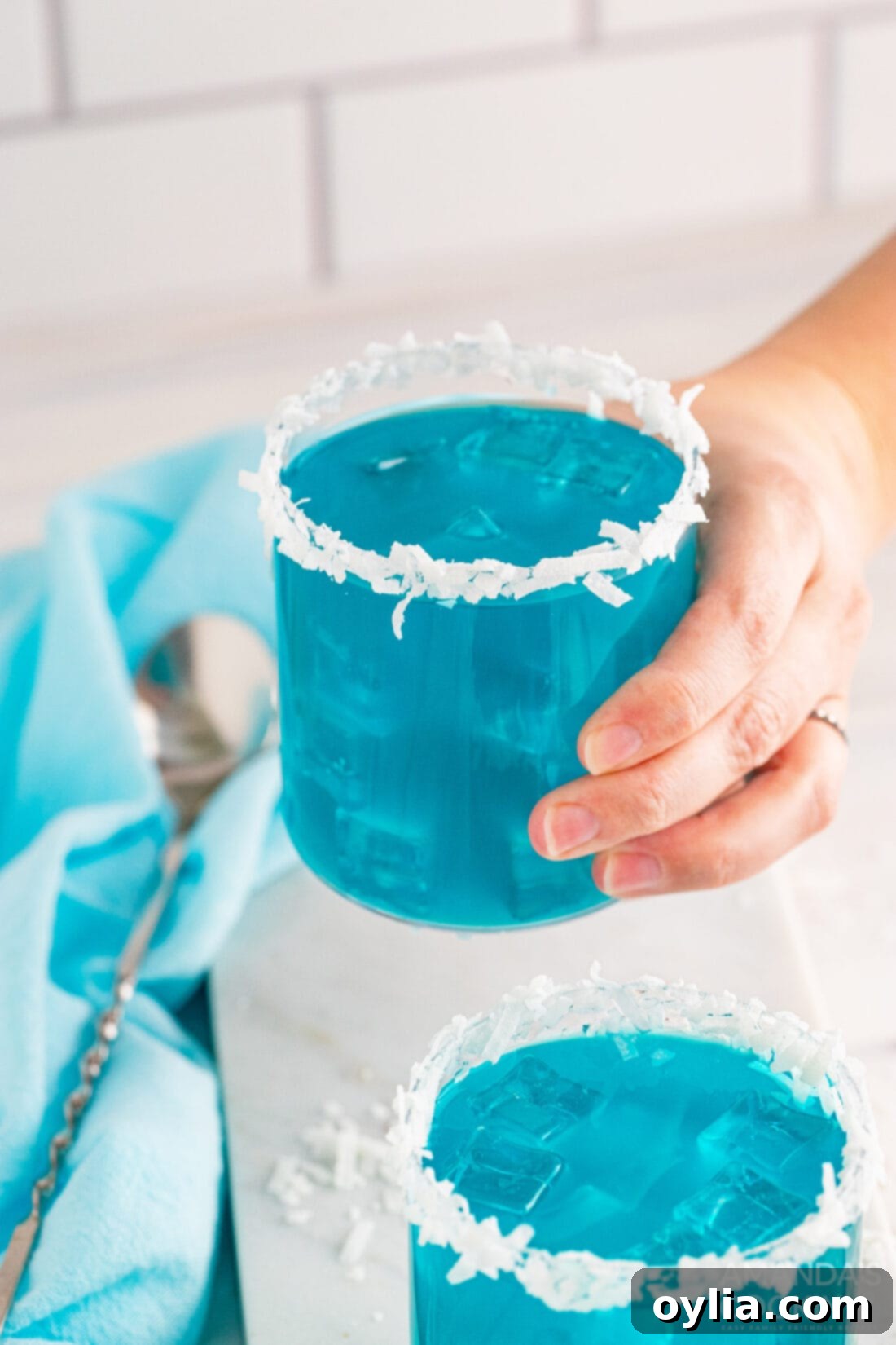 Close-up of a hand holding an Ocean Water Cocktail, showcasing its vibrant blue color and tropical allure.