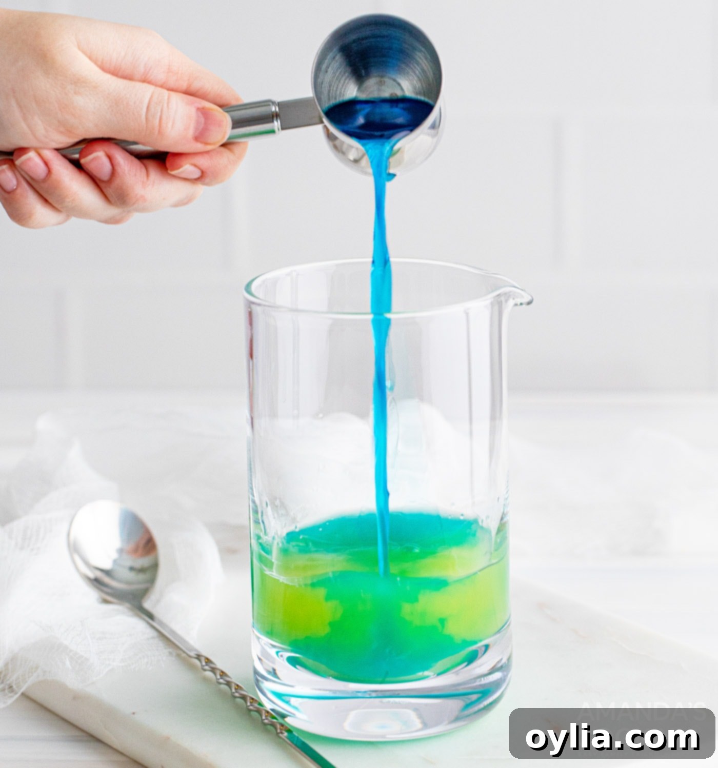adding blue curacao to a mixing glass with other cocktail ingredients