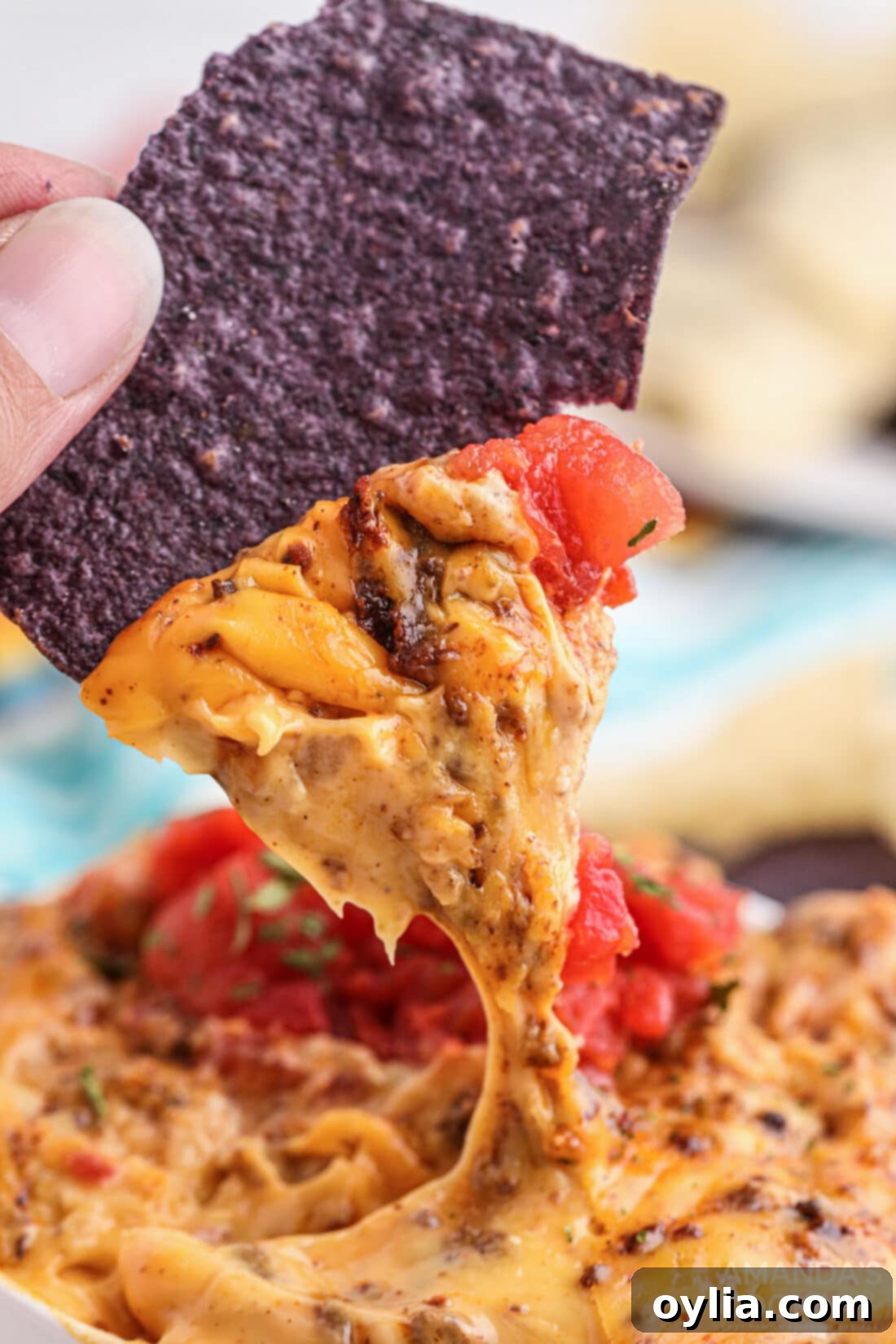 Hand dipping a tortilla chip into creamy Smoked Queso Dip