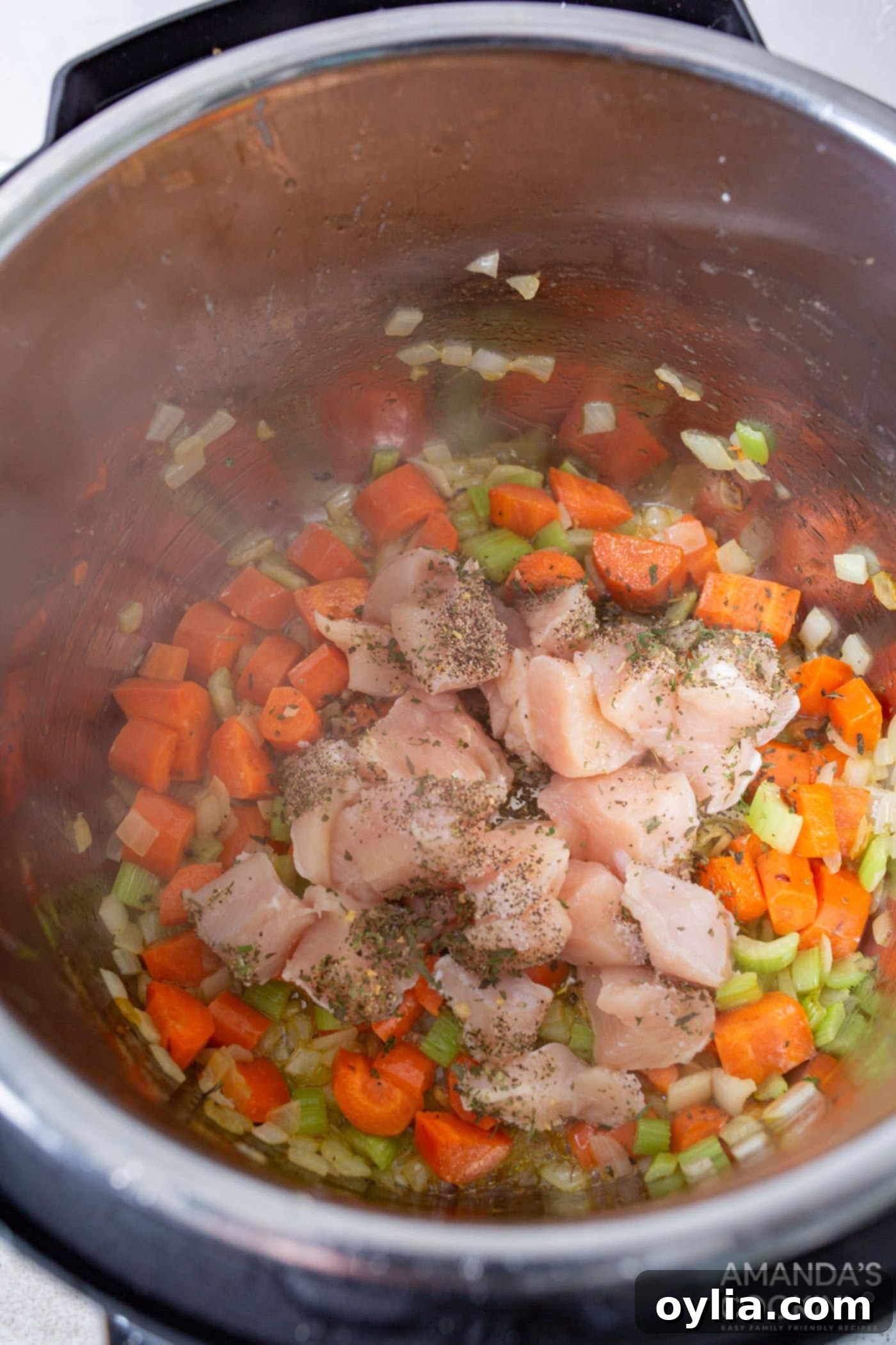 Chicken, carrots, celery, onion, and seasonings mixed in an Instant Pot, ready for the next step of adding rice.