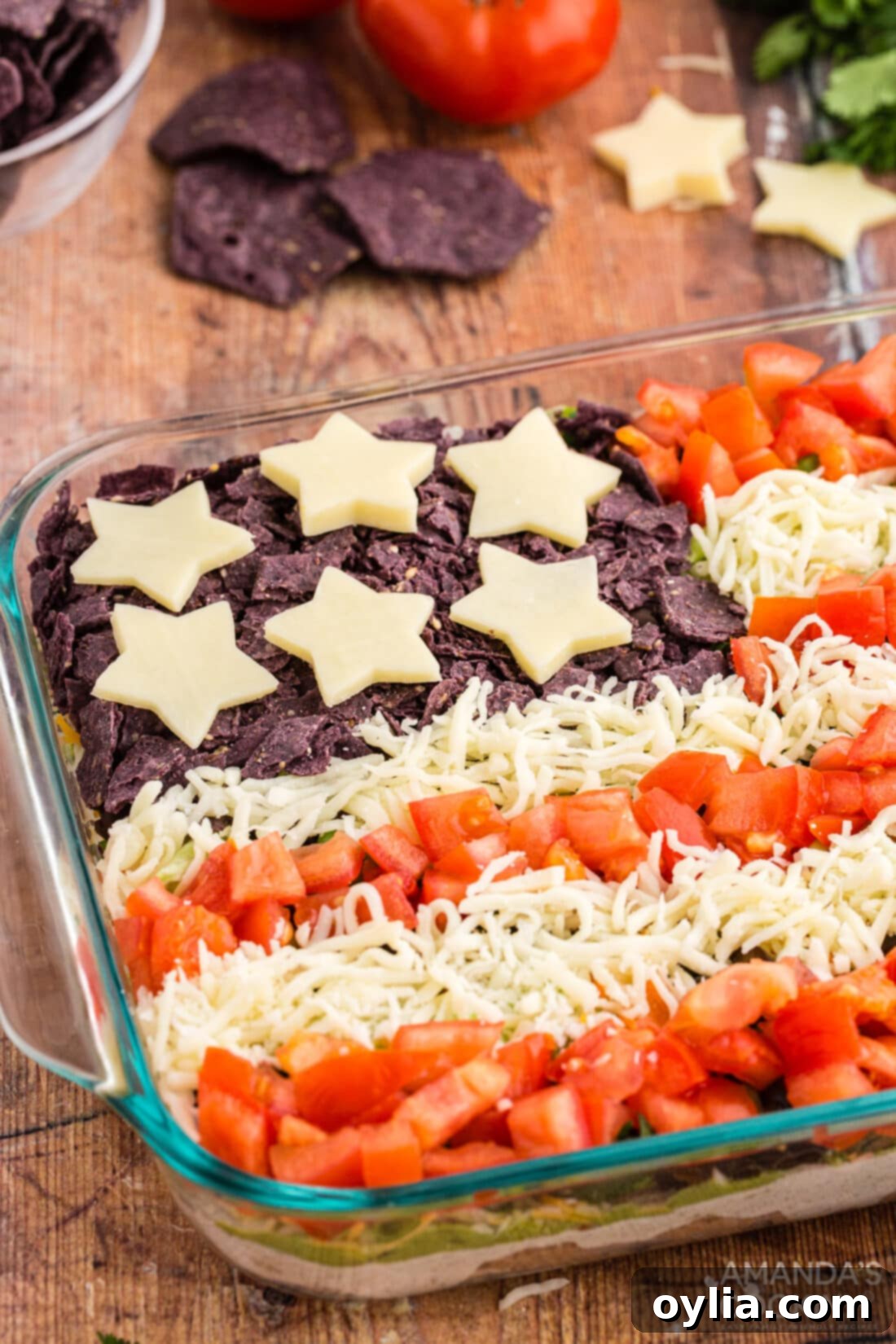 Close-up view of the Patriotic Taco Salad Flag, showing the vibrant layers of refried beans, cream cheese, guacamole, and fresh toppings, with the red and white stripes and blue chip corner clearly visible.