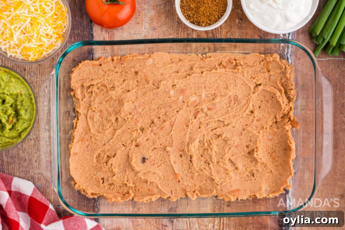 Refried beans spread evenly in a 9x13 baking dish, forming the base layer for the taco dip.