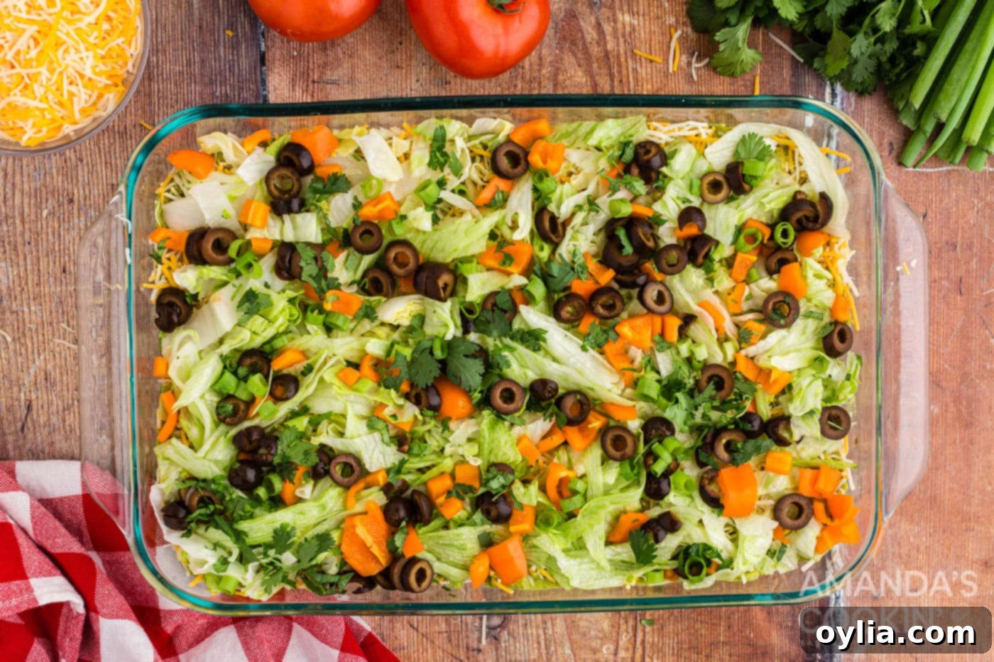 Various fresh vegetables like cheese, lettuce, green onion, bell pepper, olives, and cilantro layered on top of the guacamole, ready for the flag design.